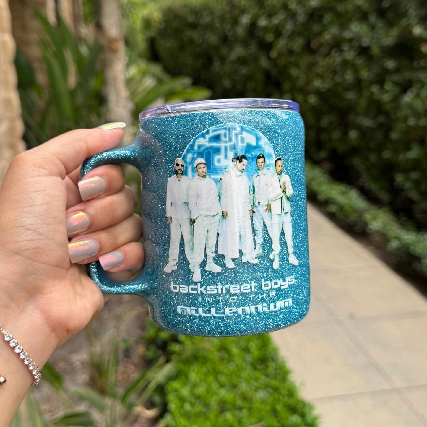 Blue glittery mug with Backstreet Boys design held by a hand outdoors.