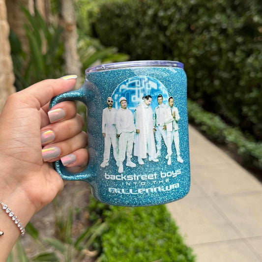 Blue glittery mug with Backstreet Boys design held by a hand outdoors.